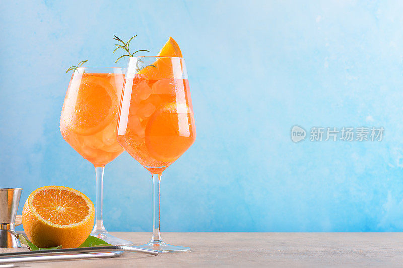 经典的意大利开胃酒aperol spritz鸡尾酒在两个杯子与冰，橙色的蓝色背景，大理石平台